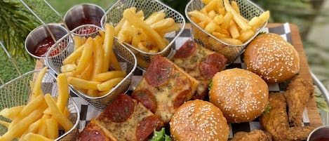 Una mesa de madera con una variedad de comidas fritas como hamburguesas, alitas de pollo y papas fritas, acompañadas de kétchup.