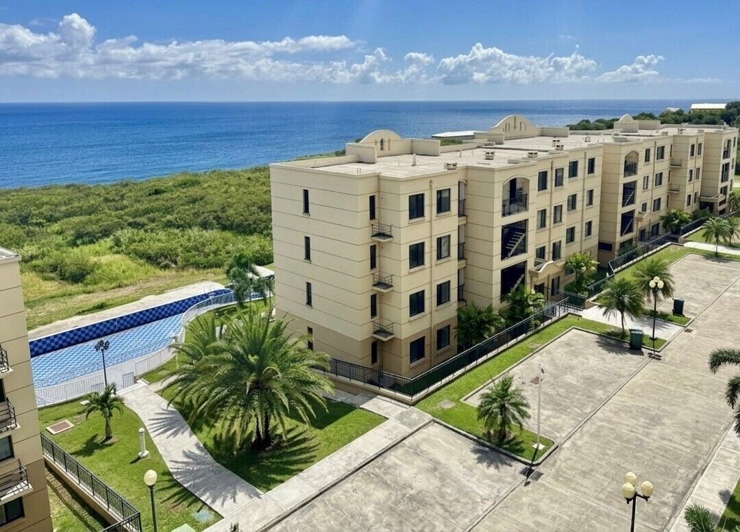 A multi-story hotel with a pool, palm trees, and a view of the ocean.