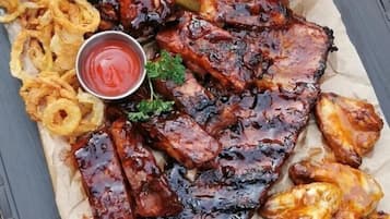 A meal consisting of ribs, wings, fries, onion rings, and two dipping sauces on a table.
