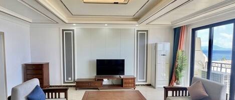 Un salón amplio con televisor de pantalla plana, mobiliario de madera y un ventanal con vistas al mar.