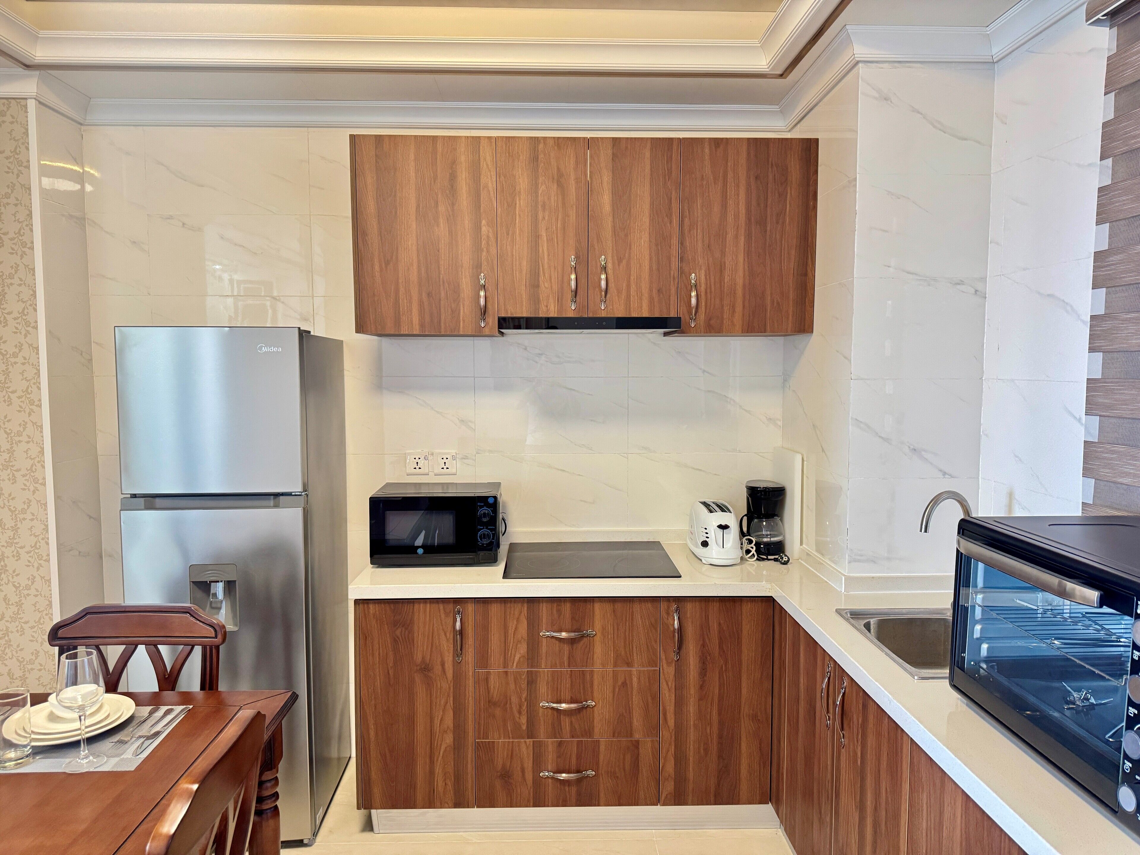 A compact kitchen with wooden cabinets, a stainless steel refrigerator, a microwave, a toaster, and a coffee maker.