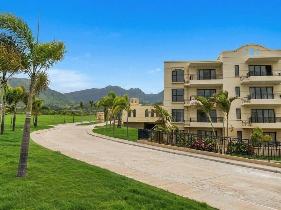Un hotel de varios pisos con un camino curvo, rodeado de palmeras y un paisaje montañoso.