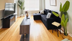 A living room with a flat-screen TV, a dark sofa, a wooden coffee table, and a large window with blinds. - Comfy home sleeps 13+ guest with wifi &parking Netflix (Brampton)