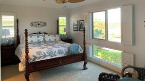 Une chambre spacieuse avec un grand lit, un ventilateur de plafond et une vue sur la verdure par la fenêtre.