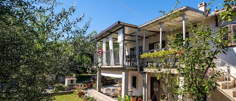Een gebouw met twee verdiepingen, voorzien van een balkon, omringd door groen en bloempotten.