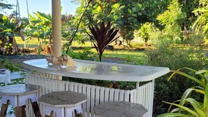 A garden patio with a white wooden table and stools, surrounded by lush greenery and plants. - Relax in this peaceful, unique getaway paradise next to the beach in Aguada. (Aguada)