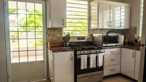 A kitchen with white cabinets, a stove, a microwave, and a window with blinds. - Relax in this peaceful, unique getaway paradise next to the beach in Aguada. (Aguada)