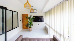 Un interior moderno con un sofá, una planta en maceta, una puerta de madera y un televisor montado en la pared.