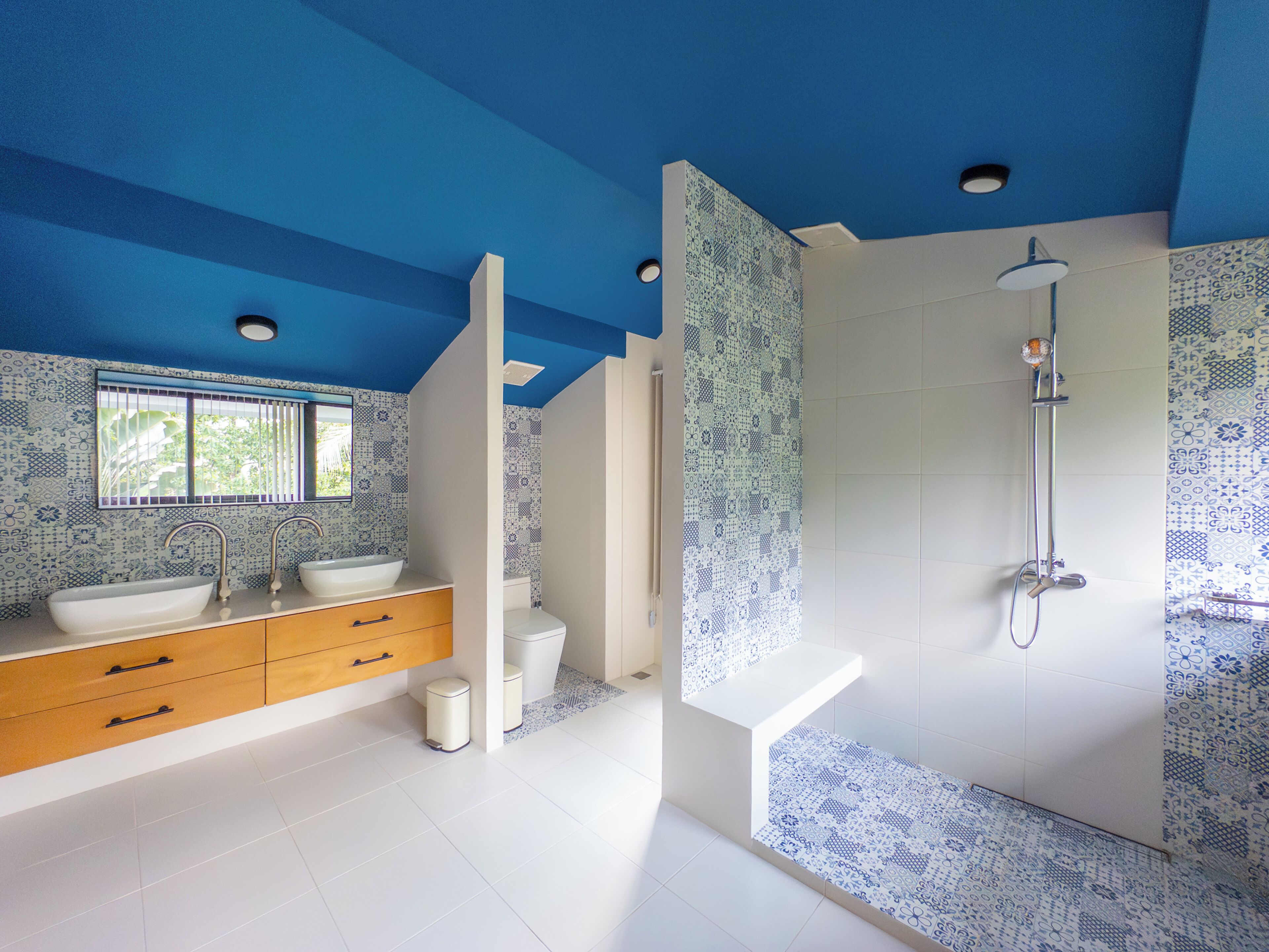 Un baño moderno con techo azul, un ventanal grande, un lavabo, un inodoro y una ducha.