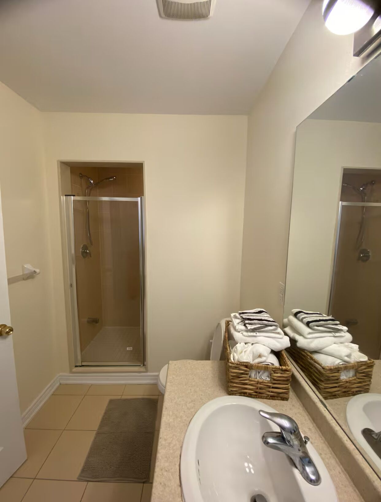 Une salle de bain dotée d’une douche à parois de verre, de deux lavabos avec miroirs et de paniers en osier contenant des serviettes pliées.