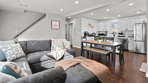 A modern living room with a grey sectional sofa, a wooden dining table, and a kitchen in the background. - #22- 4 Br 2 Ba house-Central CT (New Britain)