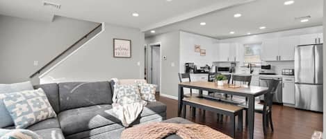 A modern living room with a grey sofa, a dining table, and a kitchen in the background.
