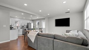A modern living room with a grey sectional sofa, a flat-screen TV mounted on the wall, and a dining area with a table and chairs. - #22- 4 Br 2 Ba house-Central CT (New Britain)