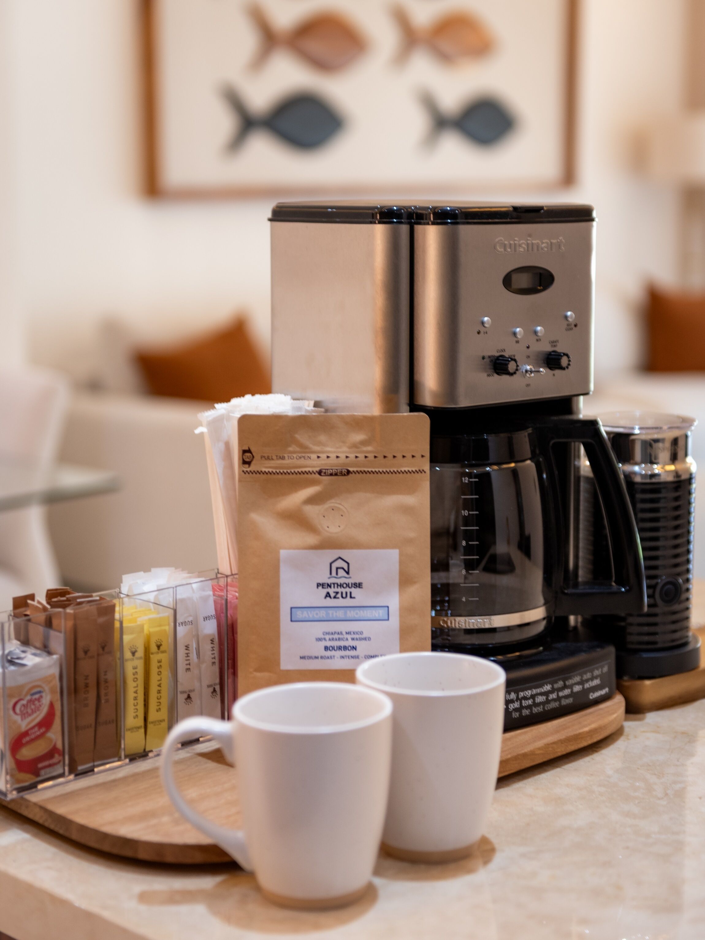Eine Kaffeemaschine, eine Packung Penthouse Azul Kaffee und zwei weiße Tassen auf einem Tablett.