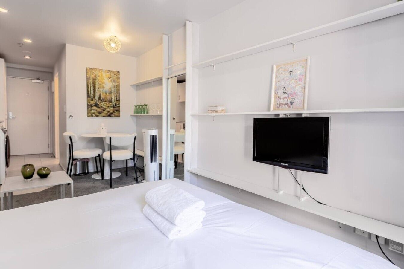 Quarto de hotel moderno com cama, televisão de tela plana, escrivaninha com cadeiras e obras de arte nas paredes.