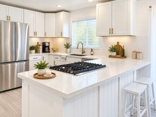 A modern kitchen with white cabinetry, stainless steel appliances, and a central island with stools. - The Guest House - Newly Remodeled (Lynnwood)