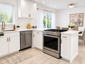 A modern kitchen with white cabinetry, stainless steel appliances, and a dining area with a table and chairs.