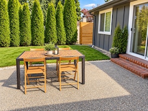 An outdoor patio with a table and chairs, surrounded by a well-maintained lawn and tall trees.