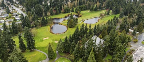 An aerial view of a golf course with multiple ponds, surrounded by dense forest and residential areas.
