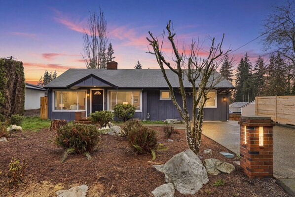 A modern two-story house with a well-maintained garden, a visible chimney, and a front porch.