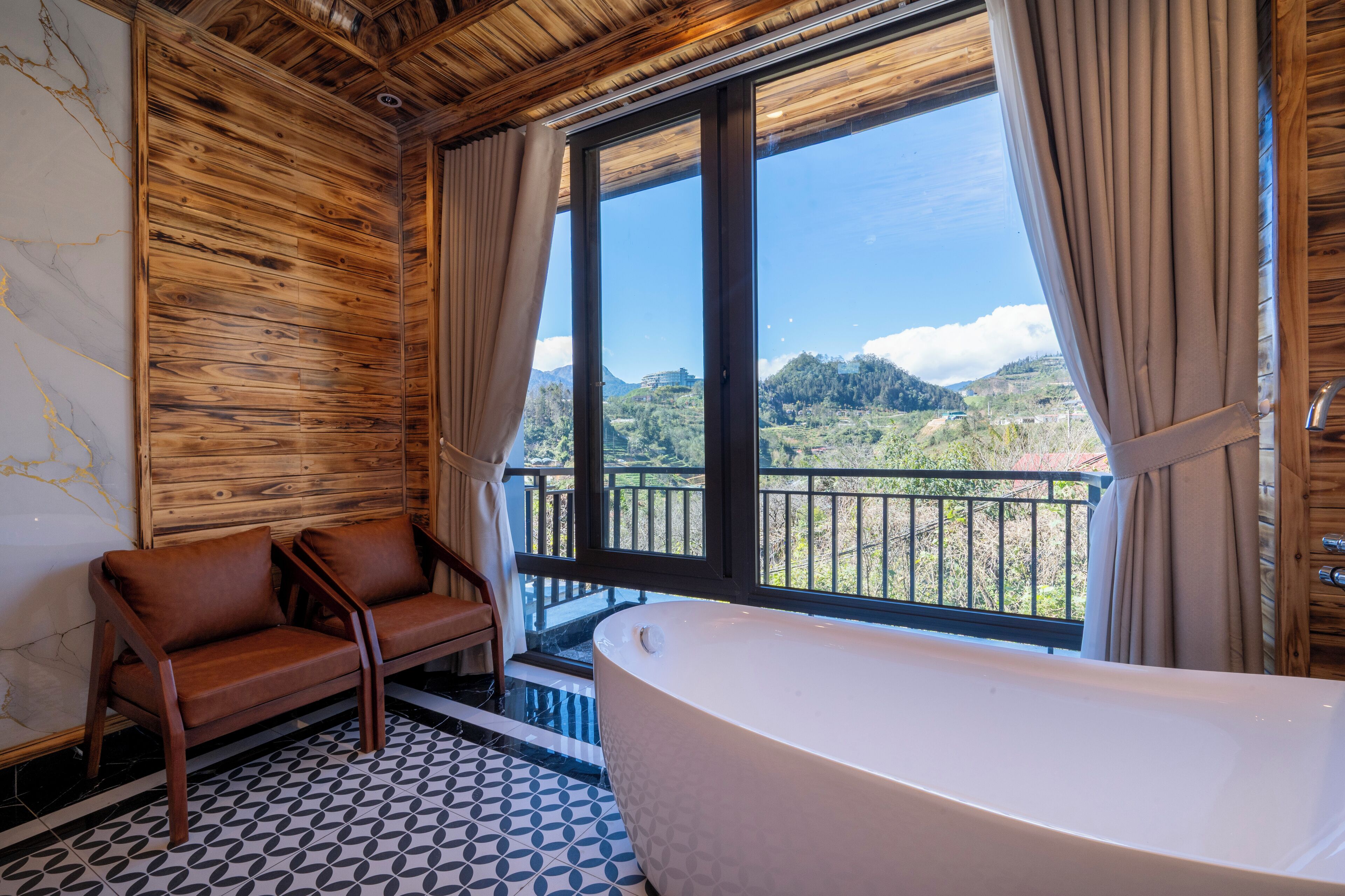 Un baño con una bañera grande, paredes de madera y vistas a un balcón con follaje.