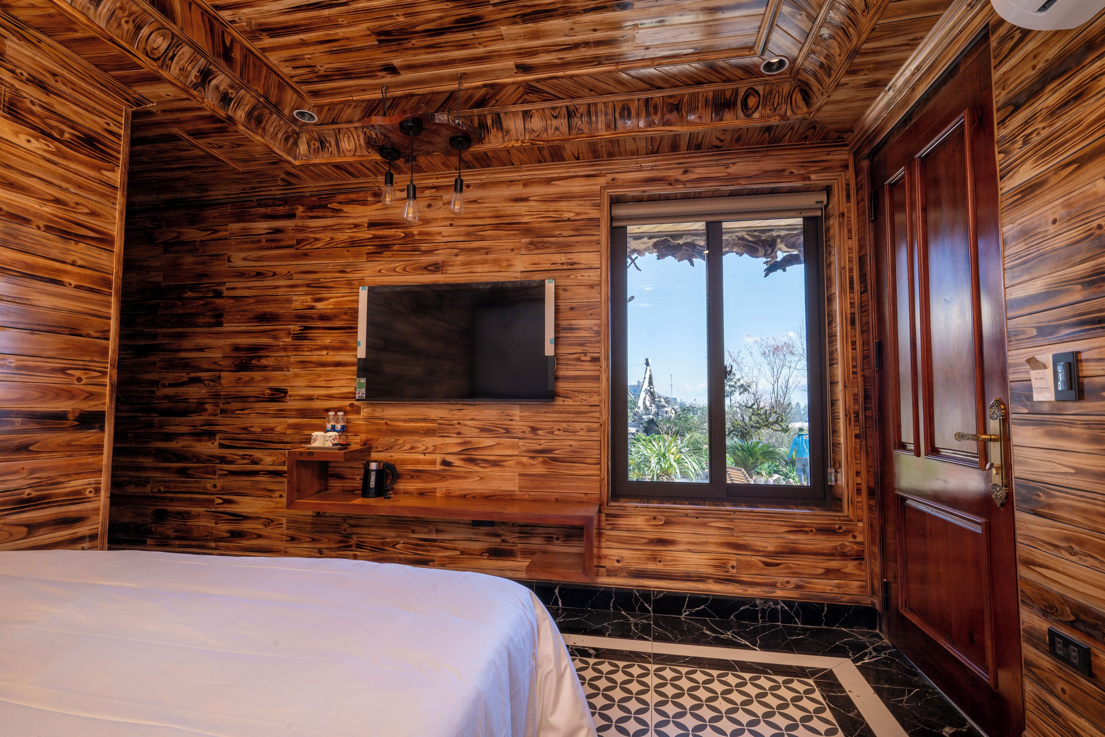 Une pièce en bois avec un lit, un téléviseur fixé au mur et une fenêtre donnant sur un paysage agréable.