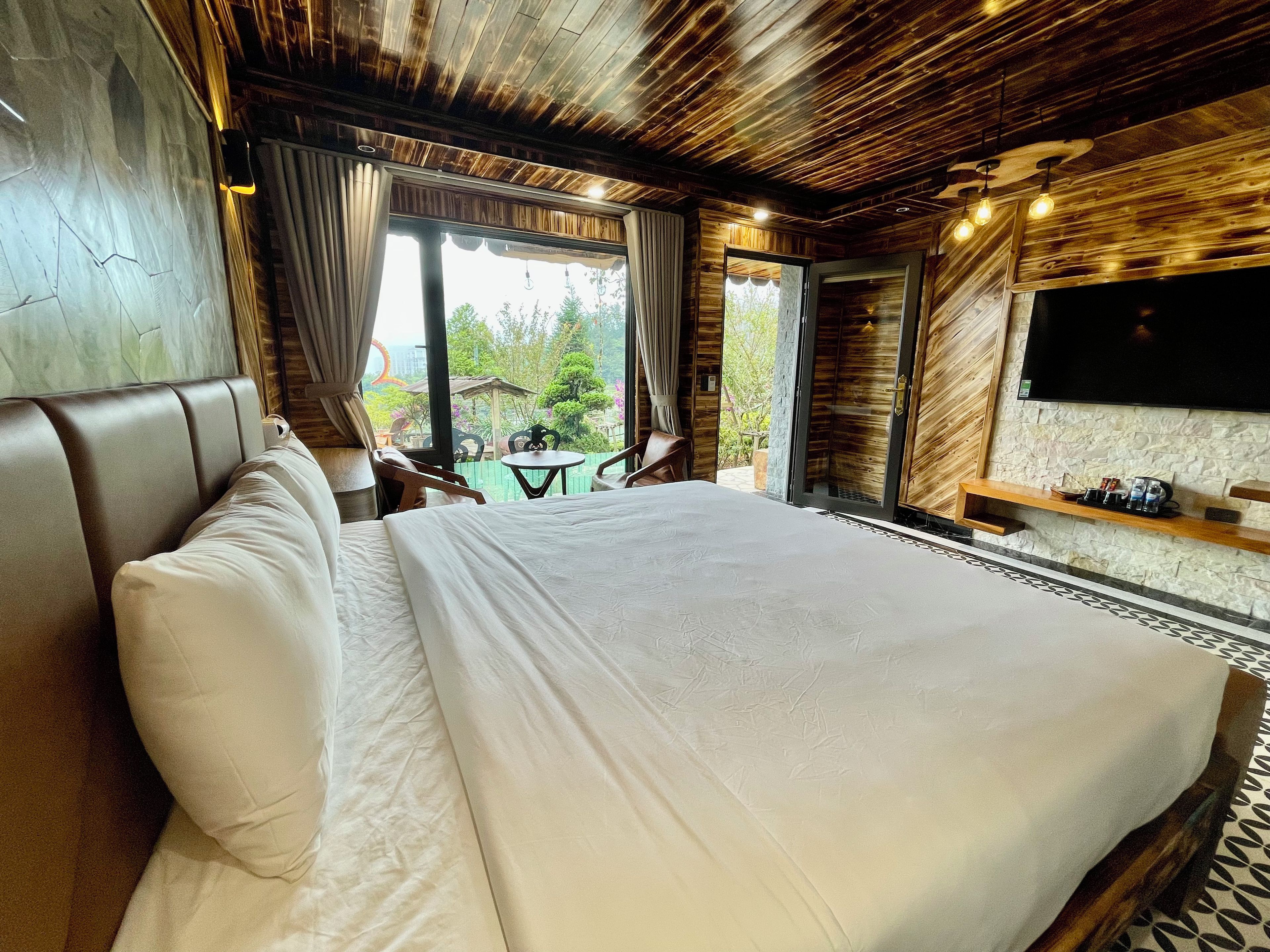 A bedroom with a large bed, a TV mounted on the wall, and a view of the outdoors.