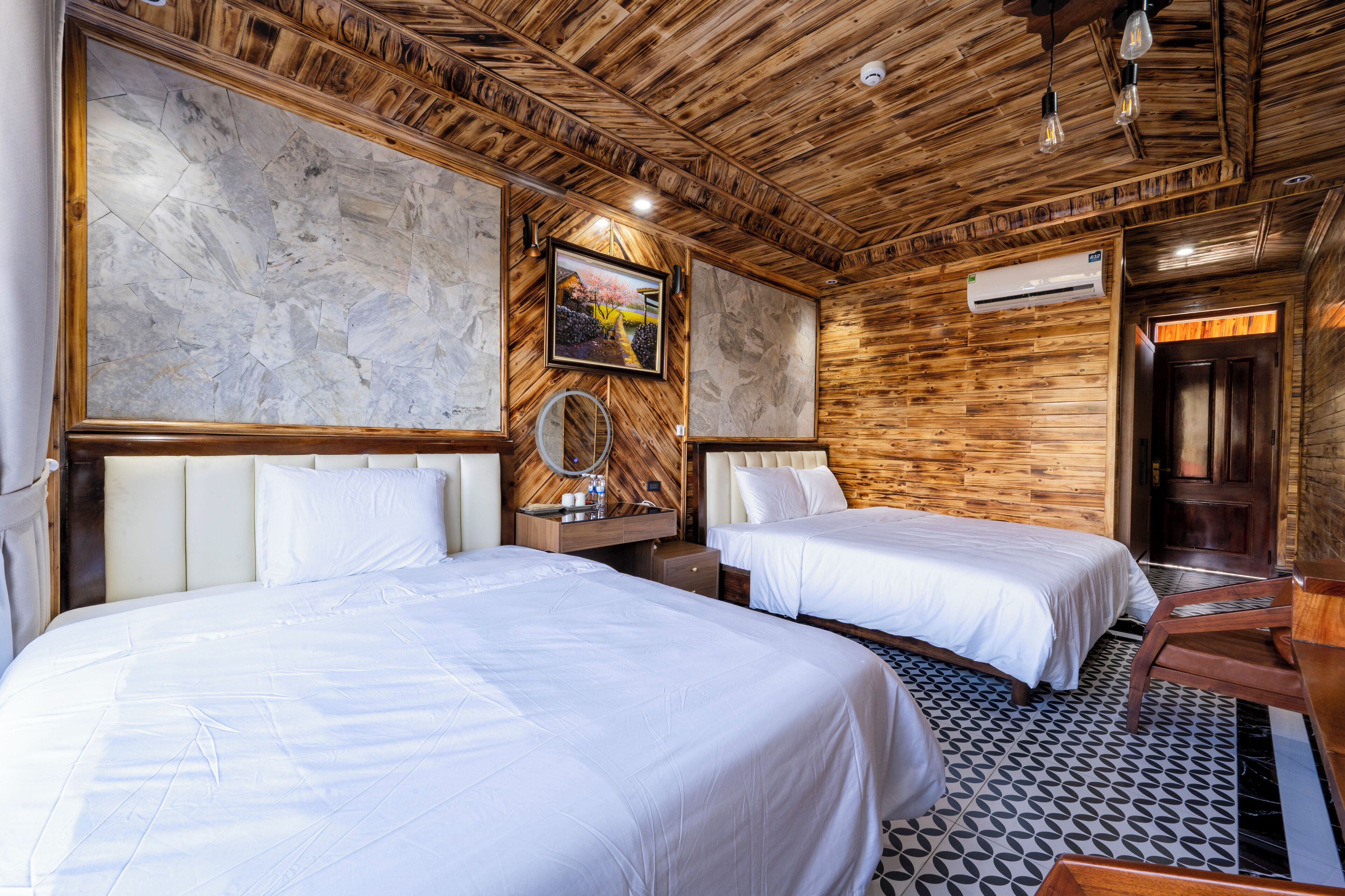 A hotel room with two beds, wooden walls, a marble accent wall, and a ceiling with exposed beams.