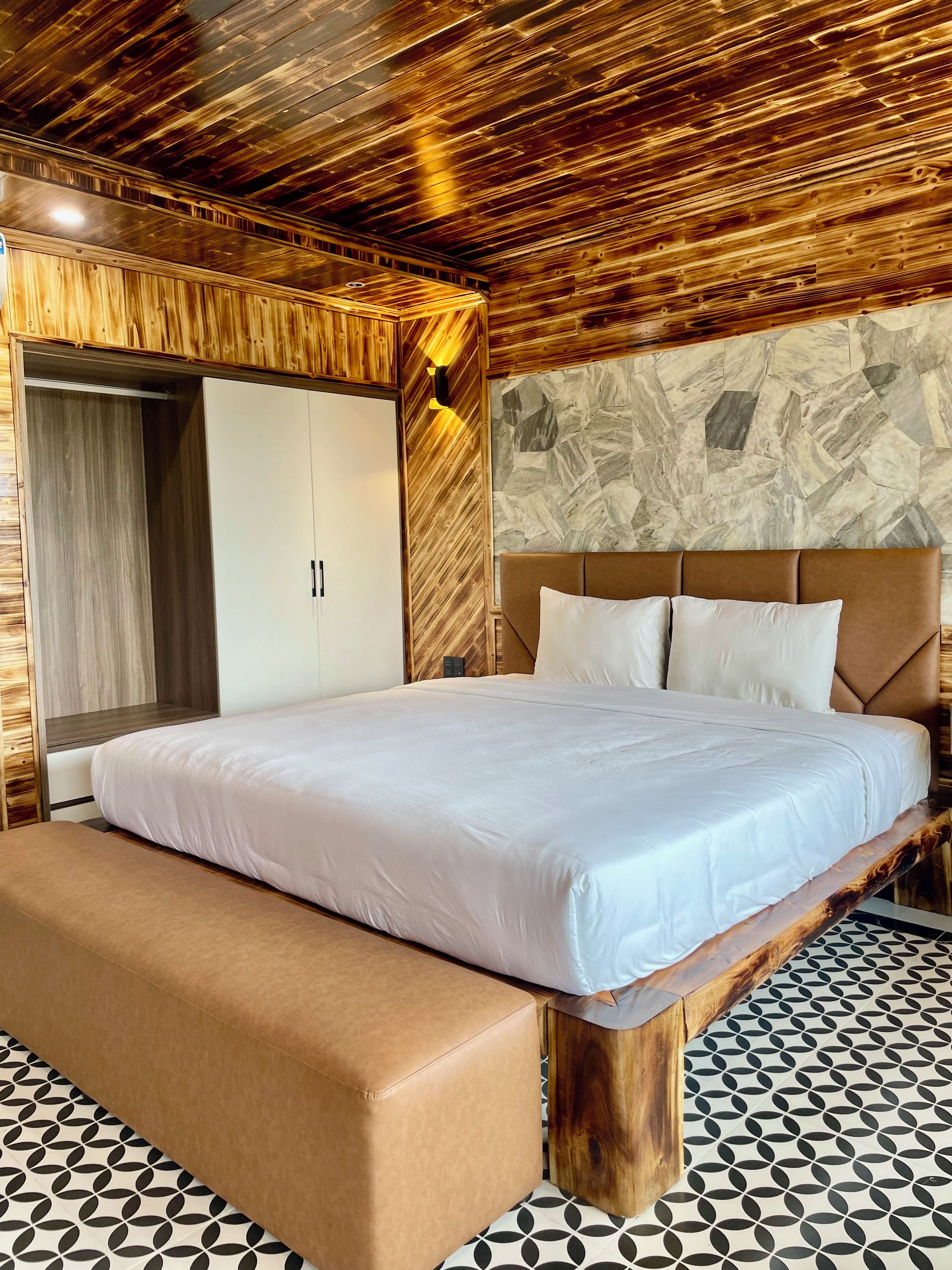 Een slaapkamer met een bed, een bankje, een kledingkast en een stenen muur.