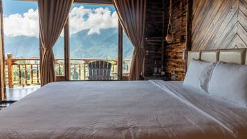 Un grand lit avec une tête de lit, des rideaux et une vue sur les montagnes depuis un balcon.