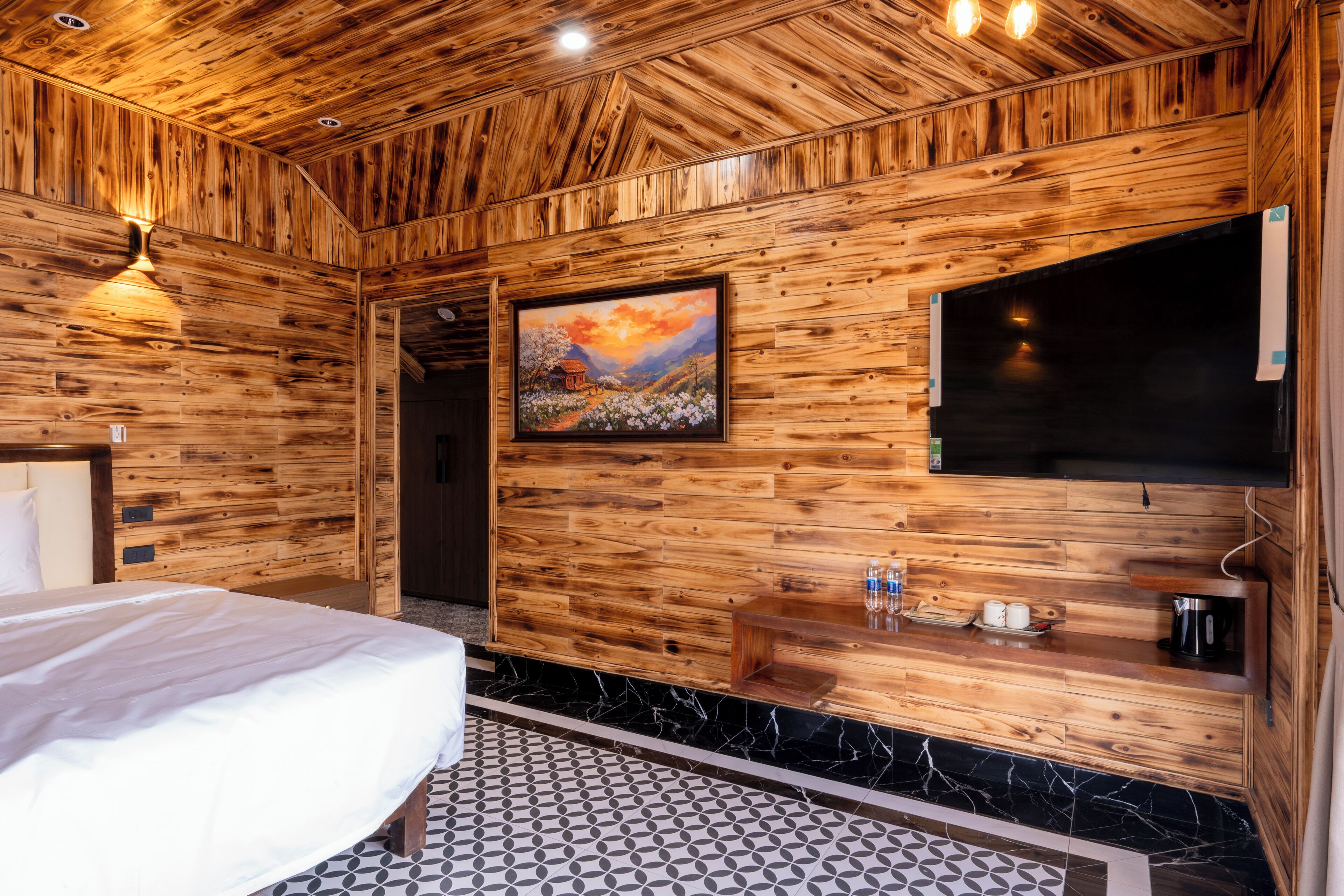 A wooden-paneled room with a bed, a painting, a TV, and a small shelf with items.