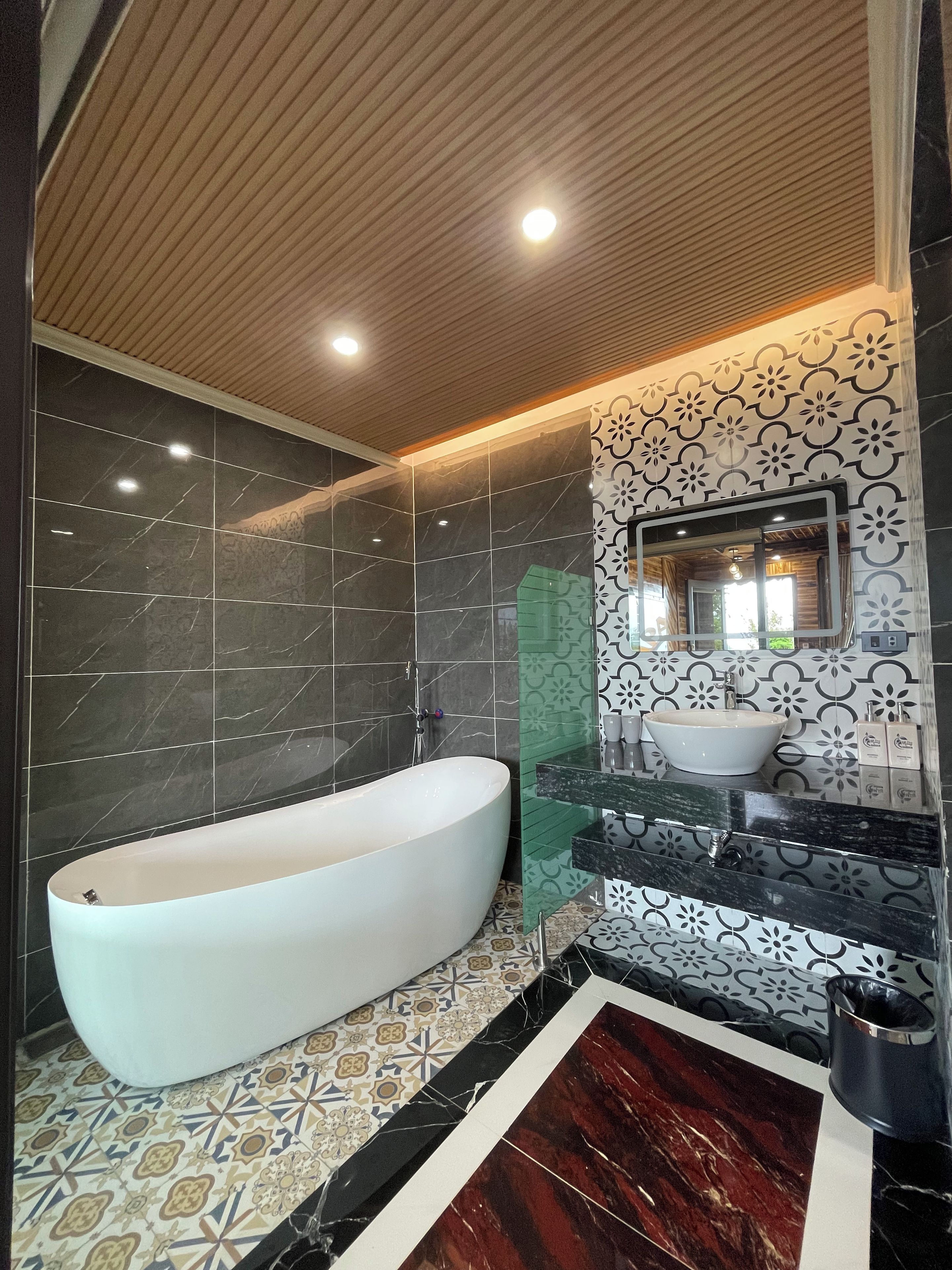 A modern bathroom with a freestanding bathtub, a vanity with a sink, and patterned tiles on the walls and floor.