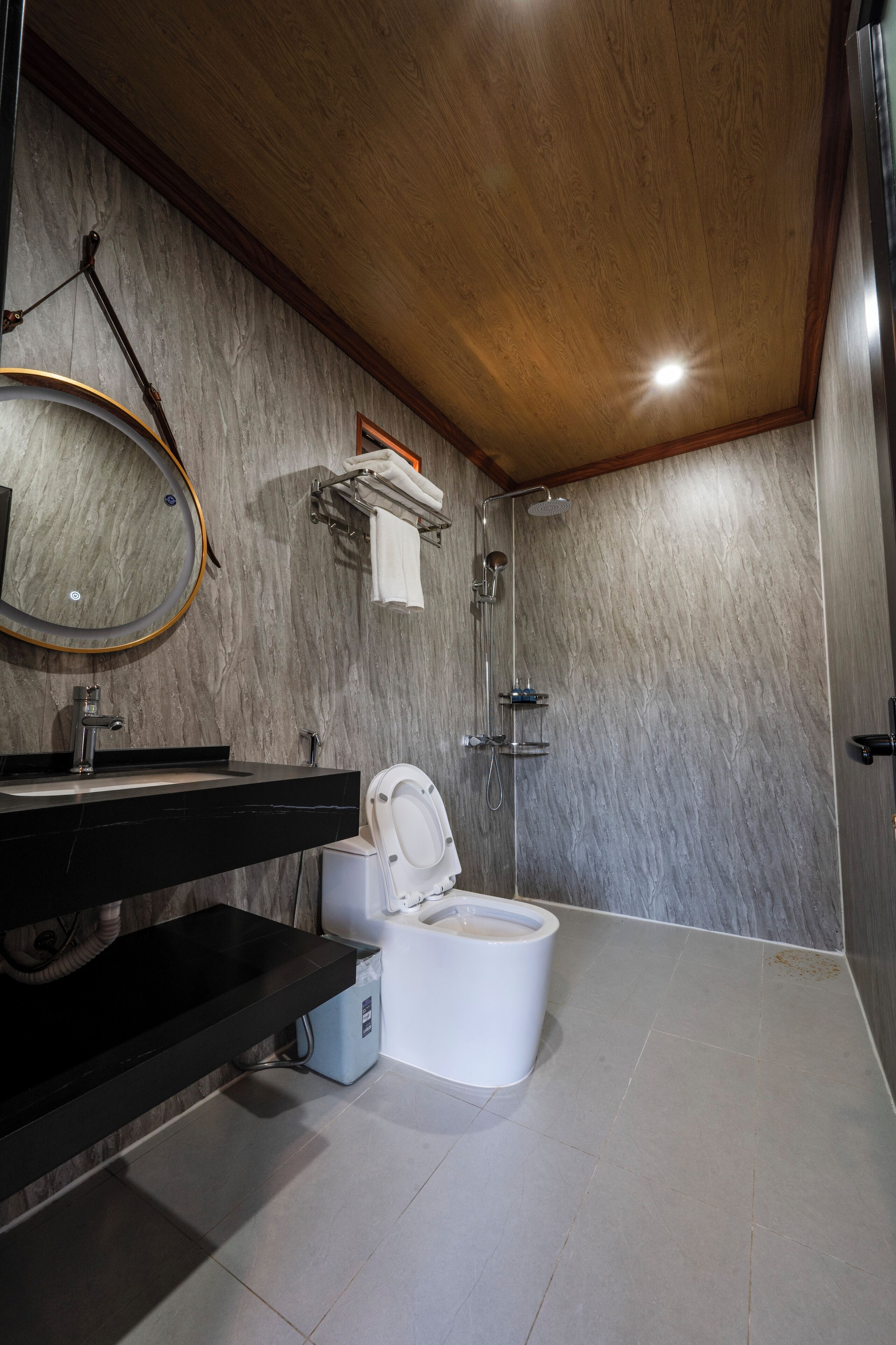 A modern bathroom with a wooden ceiling, a black sink, a white toilet, a shower, and a marble wall.