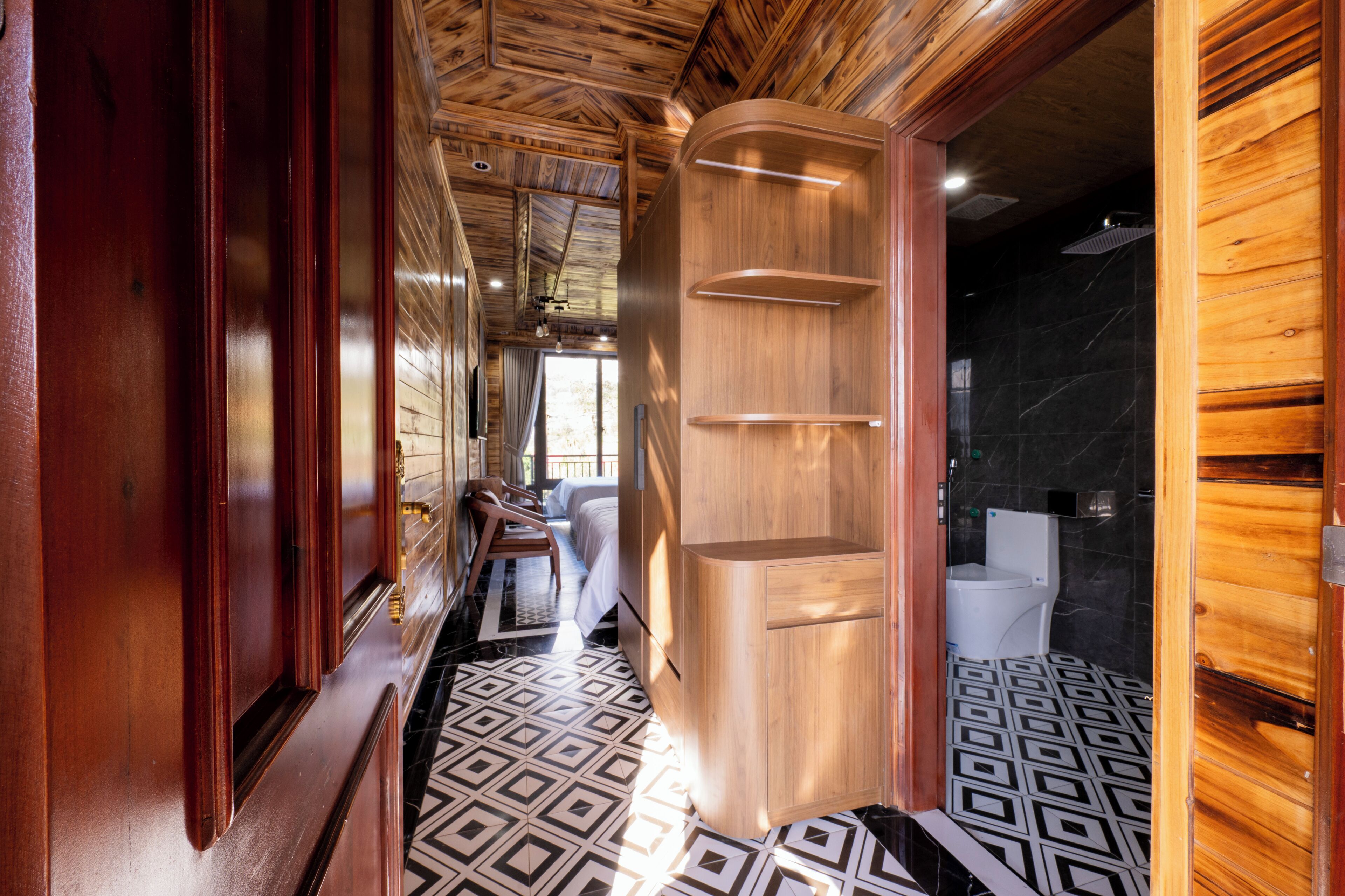 Un interior de madera con piso estampado, una cama y un baño con inodoro y lavamanos.