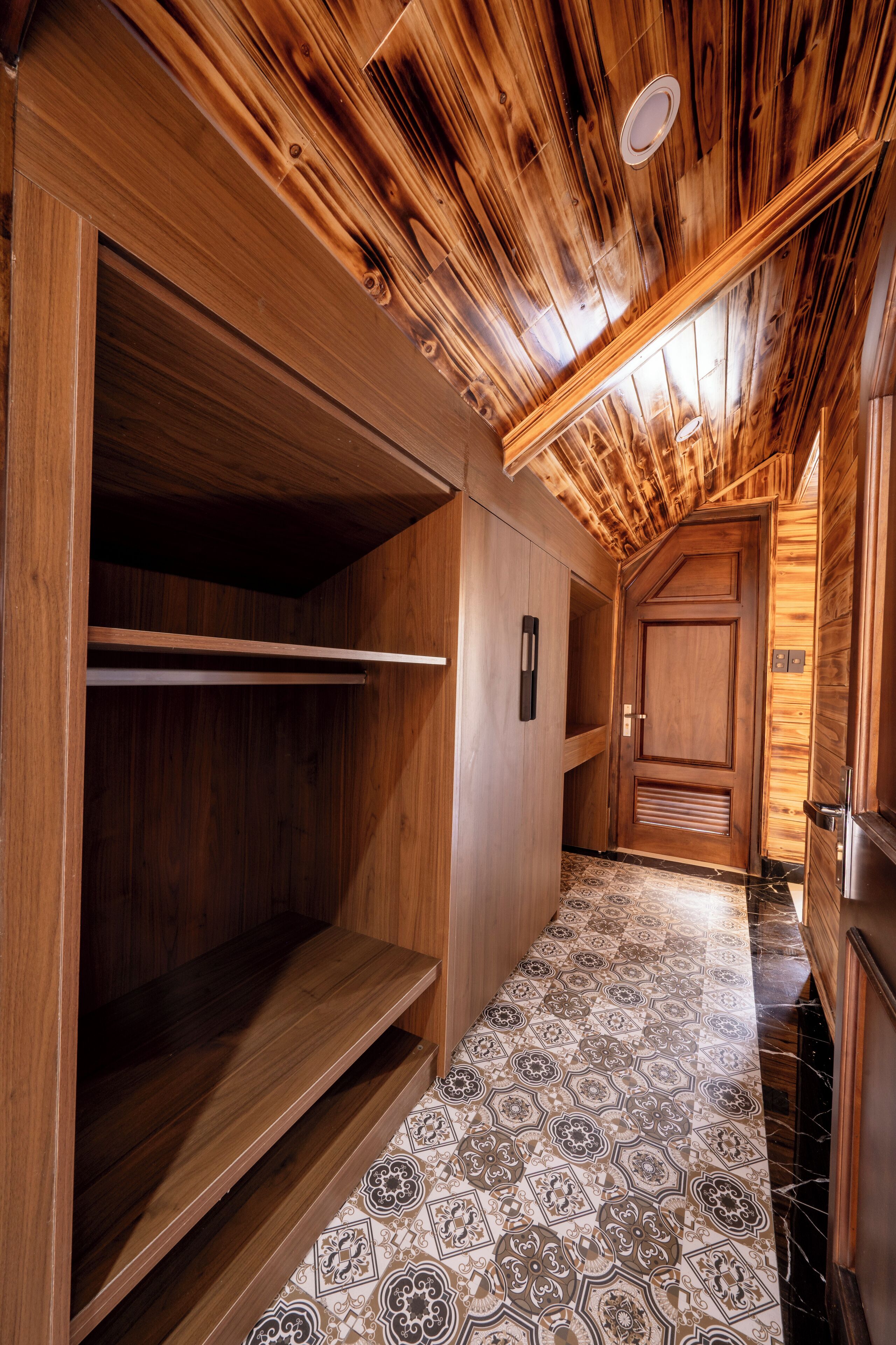 A wooden interior with a sloped ceiling, a patterned floor, and a door with a handle.