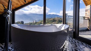 Una bañera grande y separada en un cuarto con vistas a montañas a través de amplios ventanales.