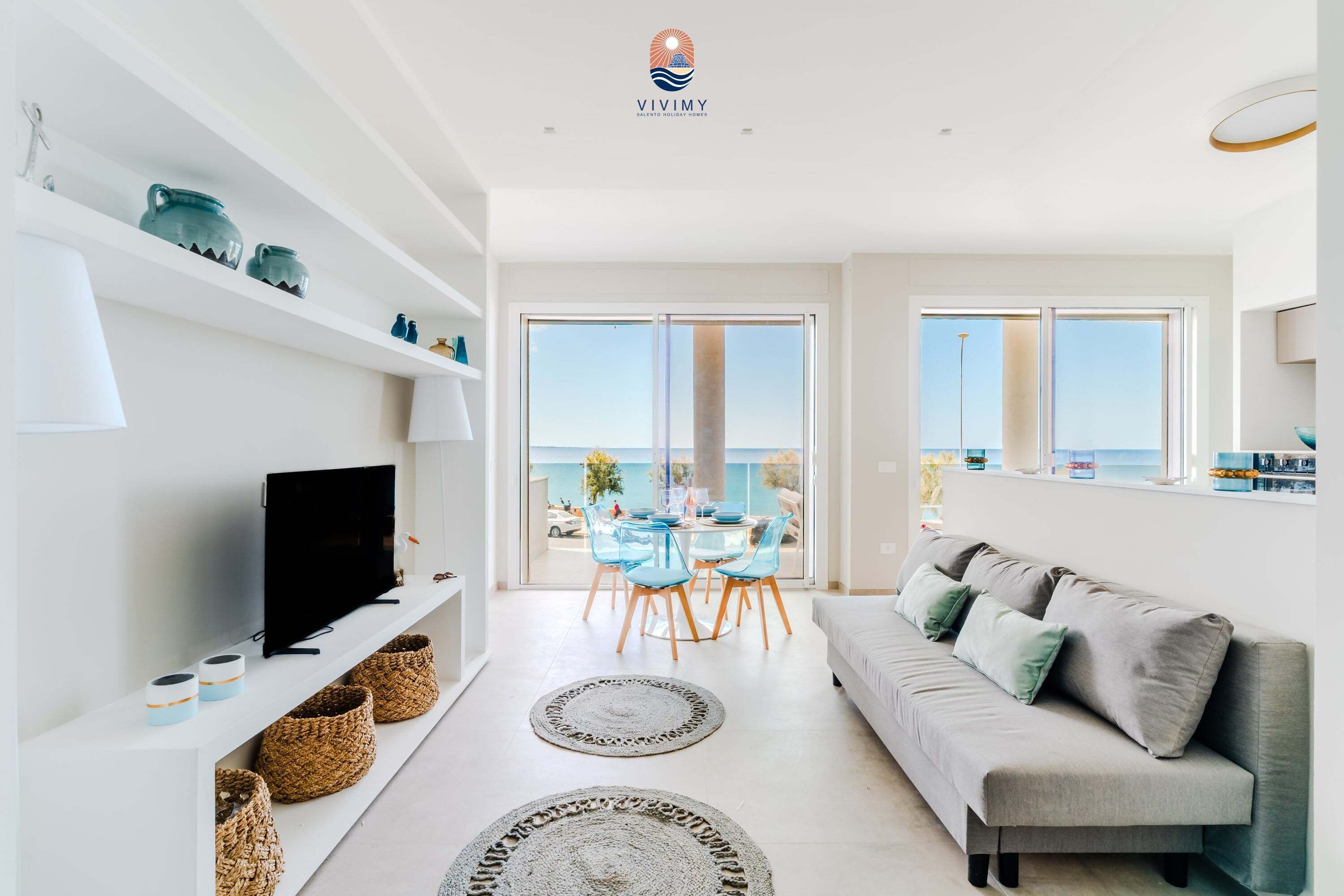 Un salon moderne comprenant un téléviseur, un canapé et un coin repas avec des chaises, donnant sur un balcon avec vue.
