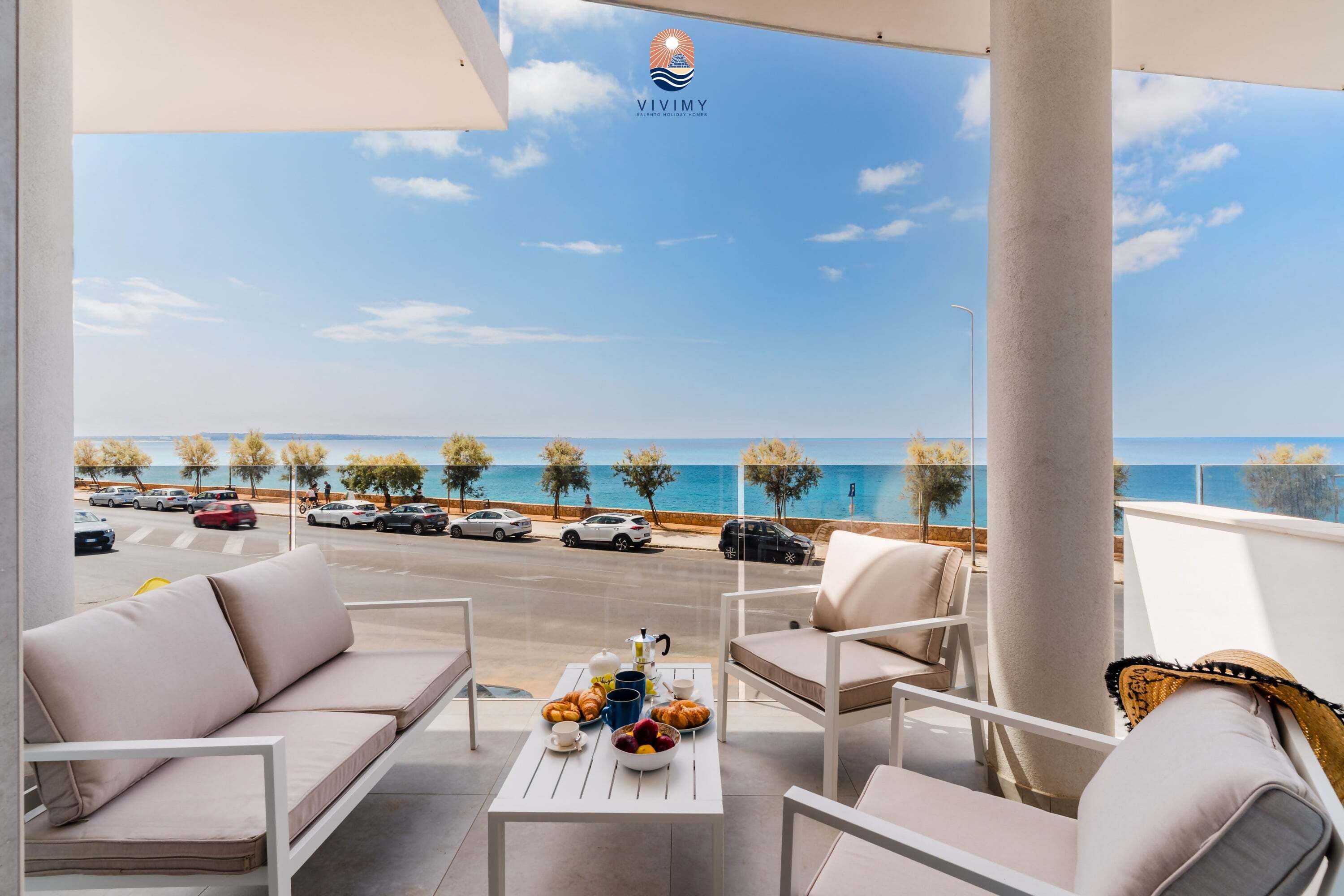 Un balcone con vista sul mare, un tavolo con prodotti per la colazione e il logo di Vivimby.