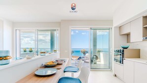 Et moderne køkken med havudsigt, et spiseområde med blå stole og en glasdør, der fører ud til en balkon.