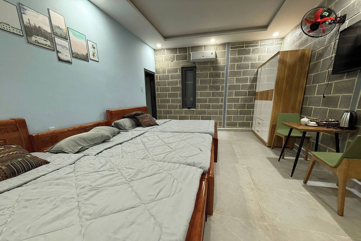 A bedroom with two beds, a small table with a kettle, and a chair.