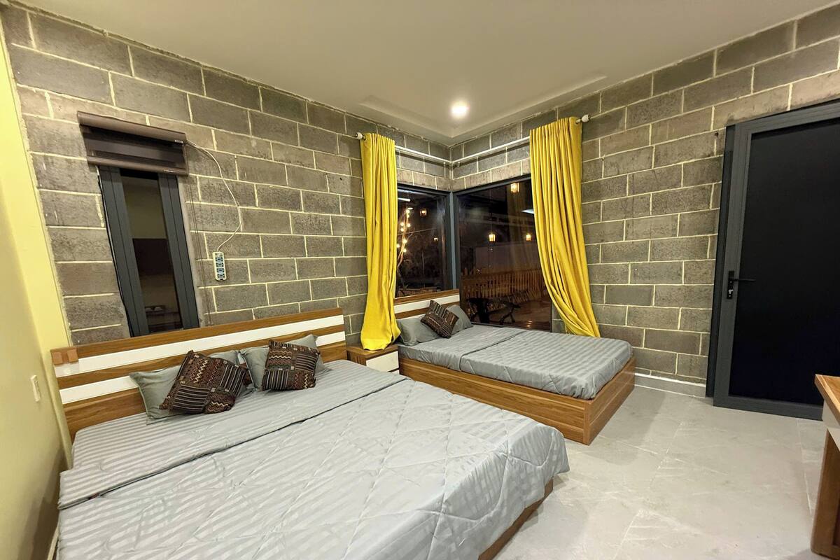 A bedroom with two beds, a stone wall, a window with curtains, and a door.