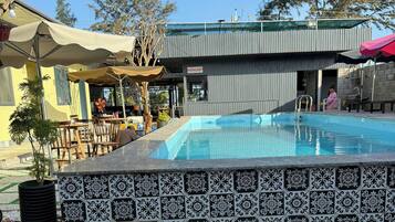 Una piscina con borde de azulejos, rodeada por una zona de patio con mobiliario exterior y una sección cubierta.