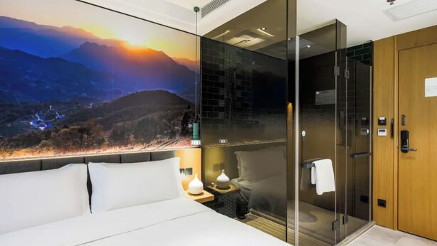 Ein modernes Hotelzimmer mit einem großen Bett, einer Glaseinteilung und Blick auf eine Berglandschaft.