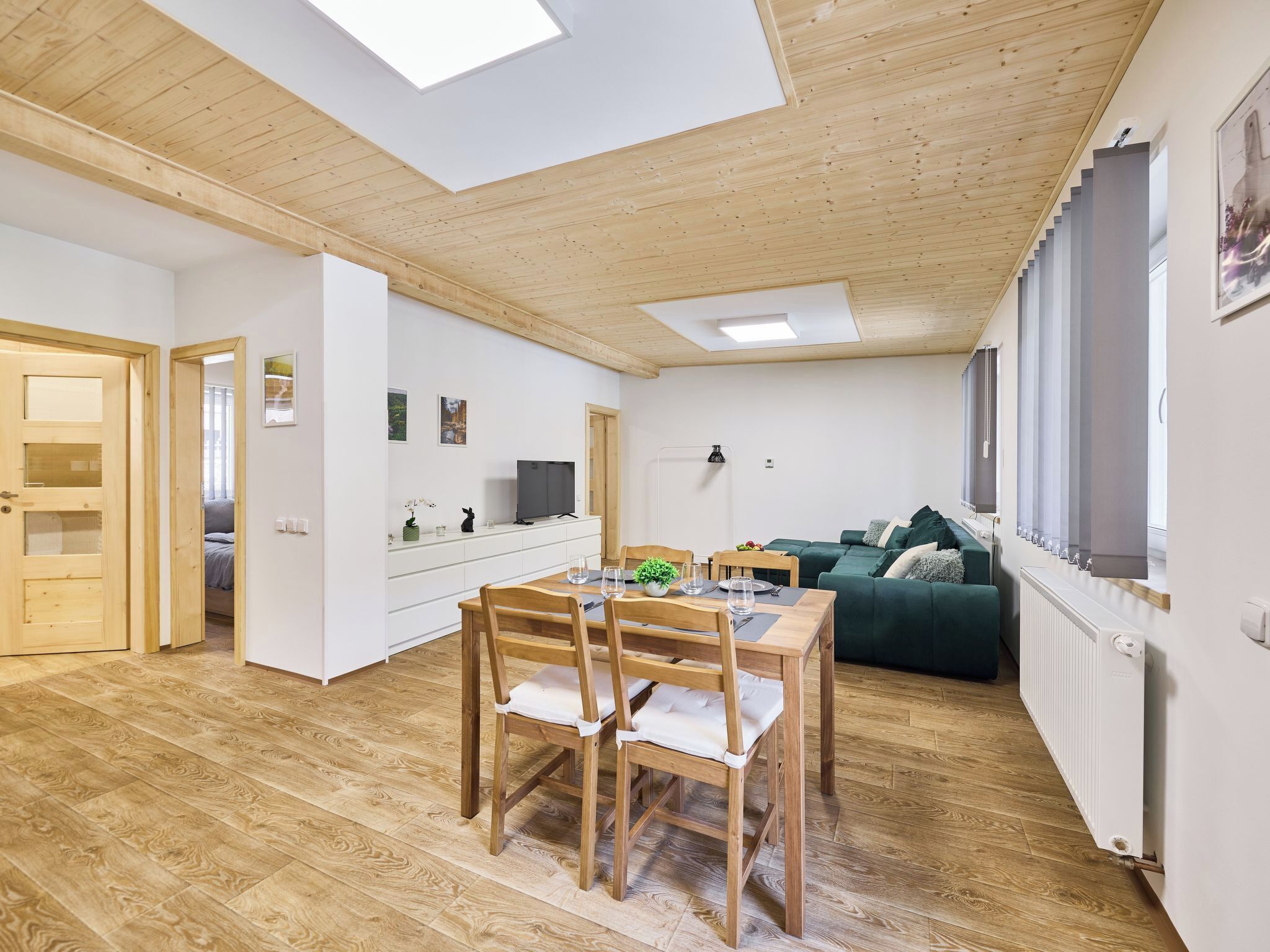 Ein modernes Interieur mit Essbereich, einer Couch, einem Fernseher und einem Fenster mit Jalousien.