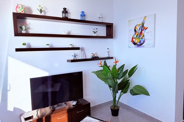 Ein Wohnzimmer mit Flachbildfernseher, Holzregalen mit Dekoration, einer Zimmerpflanze und einem Wandbild.