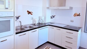 A modern kitchen with white cabinets, a black countertop, and a built-in oven. There are two sinks, a coffee maker, and a kettle. - Home Sweet Home by the Sea 060 (Durrës)