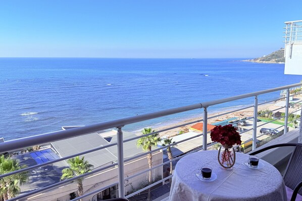 A balcony with a table, a vase with flowers, and a view of the ocean and beach. - Home Sweet Home by the Sea 060 (Durrës)