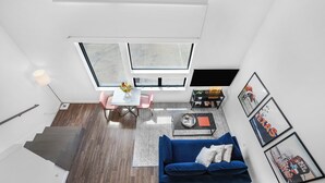 En moderne stue med en blå sofa, et sofabord og et fjernsyn. Der er en trappe til et øvre plan, og et vindue med udsigt ud.