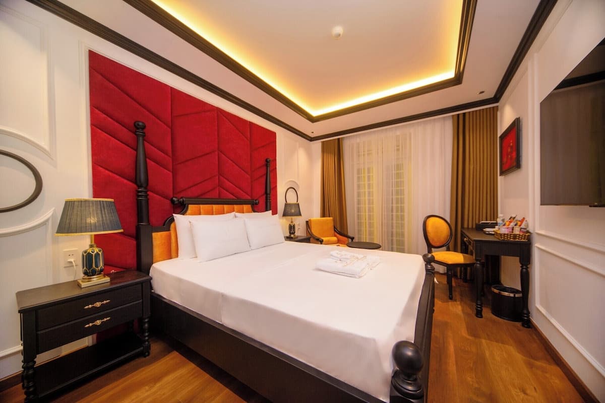 Ein Hotelzimmer mit einem großen Bett, einer roten Akzentwand, einem Holznachttisch, einem Schreibtisch und einem Sessel.