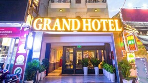Een hotel met een opvallend bord met de tekst 'GRAND HOTEL', meerdere verdiepingen en een balkon op de tweede etage.
